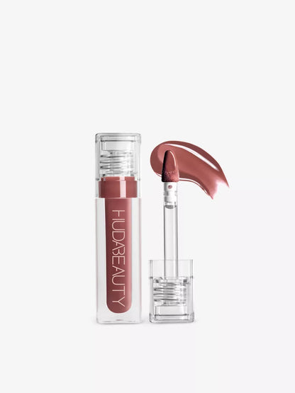 Huda beauty faux filler extra shine lip gloss tube with a clear cap, accompanied by a doe-foot applicator and a swatch of rose-pink lipstick.