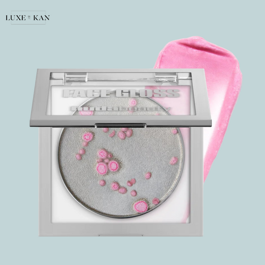 A stylish compact of huda beauty icy nude ph face gloss featuring a shimmering silver powder with pink accents and a pink applicator swatch.
