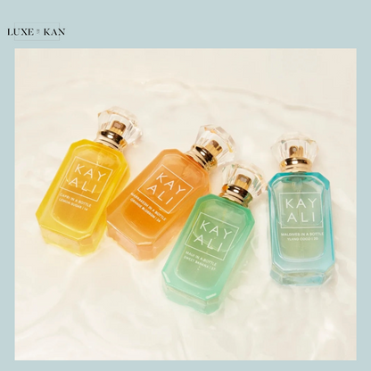 Four colorful KAYALI perfume bottles—yellow, orange, green, and blue—arranged stylishly on a soft, white surface.