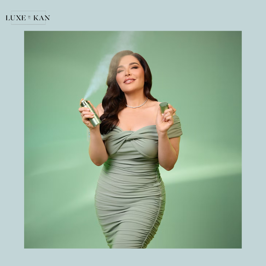 A woman in a fitted, sage green dress holds a spray can and a small container against a soft green background, exuding elegance.