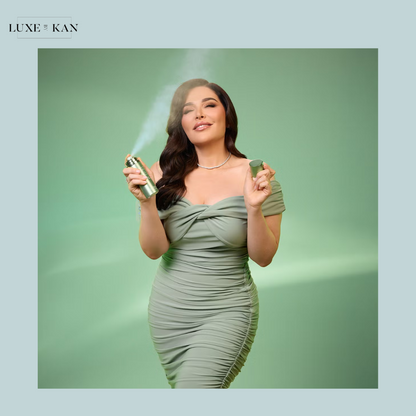 A woman in a fitted, sage green dress holds a spray can and a small container against a soft green background, exuding elegance.