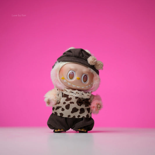Labubu doll in cocoa cuddle three-piece set, featuring a brown hat with pompoms, a brown and white patterned vest, and brown corduroy pants.