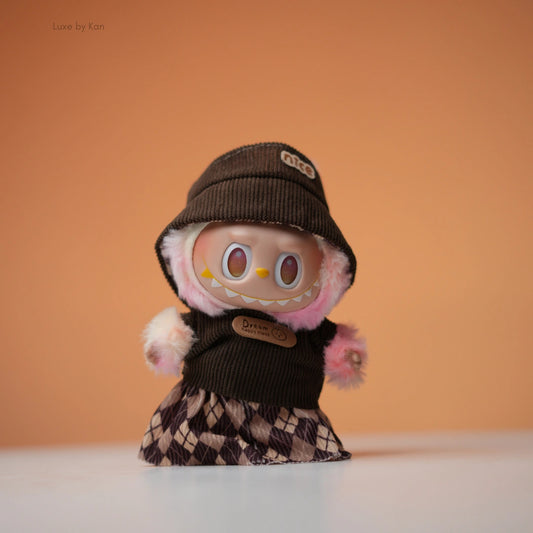 The Labubu doll wears a cozy two-piece streetwear set, including a corduroy hat and a dress adorned with a diamond argyle pattern.