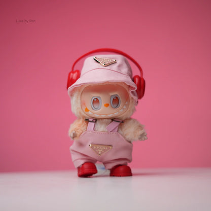 Labubu doll wearing a light pink Prada-branded bucket hat, matching overalls, red shoes, and red headphones.