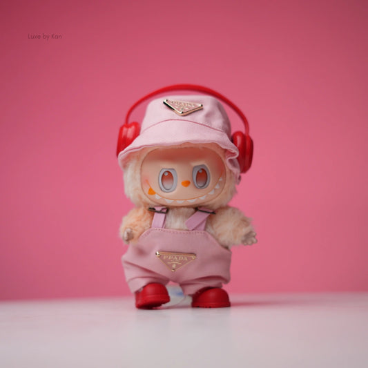 Labubu doll wearing a light pink Prada-branded bucket hat, matching overalls, red shoes, and red headphones.