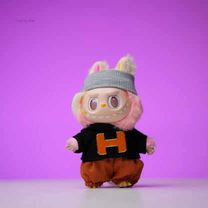 Labubu doll wearing a beanie, black sweater with an orange “H”, and brown bloomers.
