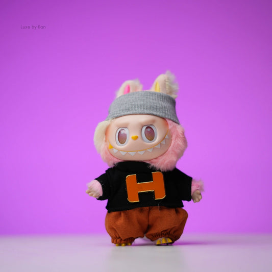 Labubu doll wearing a beanie, black sweater with an orange “H”, and brown bloomers.