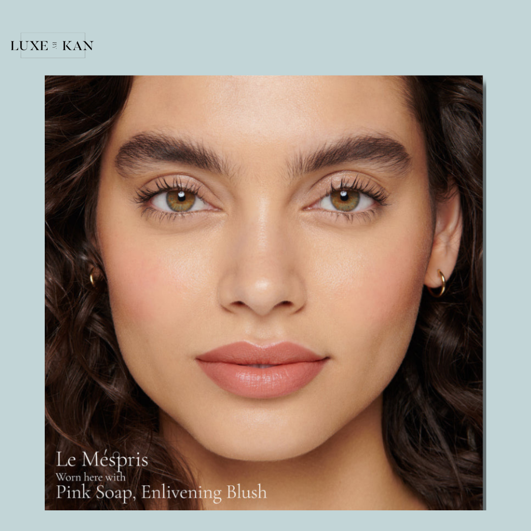 A model with curly hair and gold hoop earrings, showcasing beauty products titled "Le Mespris," "Pink Soap," and "Enlivening Blush."