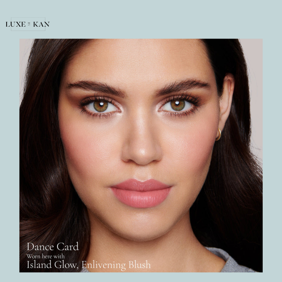 Smoky hair frames the subject's features, showcasing a fresh makeup look with the caption "Dance Card." Featuring Island Glow blush.