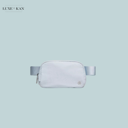 A sleek white fanny pack with a light blue strap, featuring a minimalist design and a small logo.