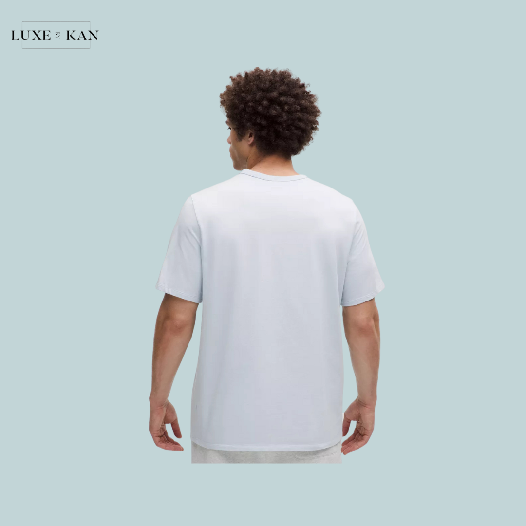 A man with curly hair stands facing away, wearing a light blue T-shirt.