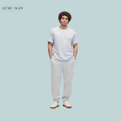 A person stands confidently in a light blue t-shirt and gray sweatpants, paired with white sneakers.