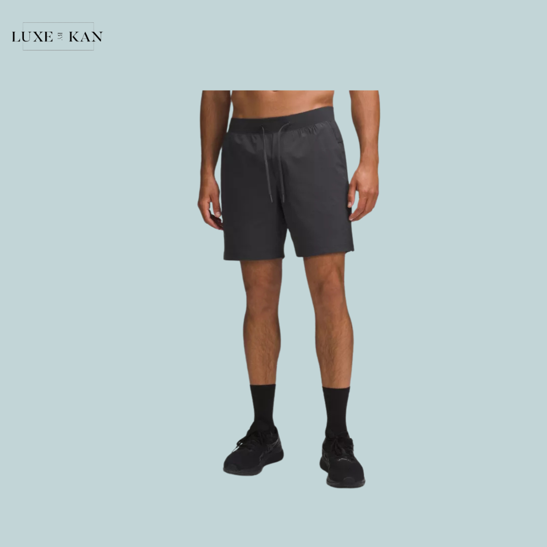 A man wearing black athletic shorts, black socks, and sneakers, standing against a light blue background with a "Luxe & Kan" logo.