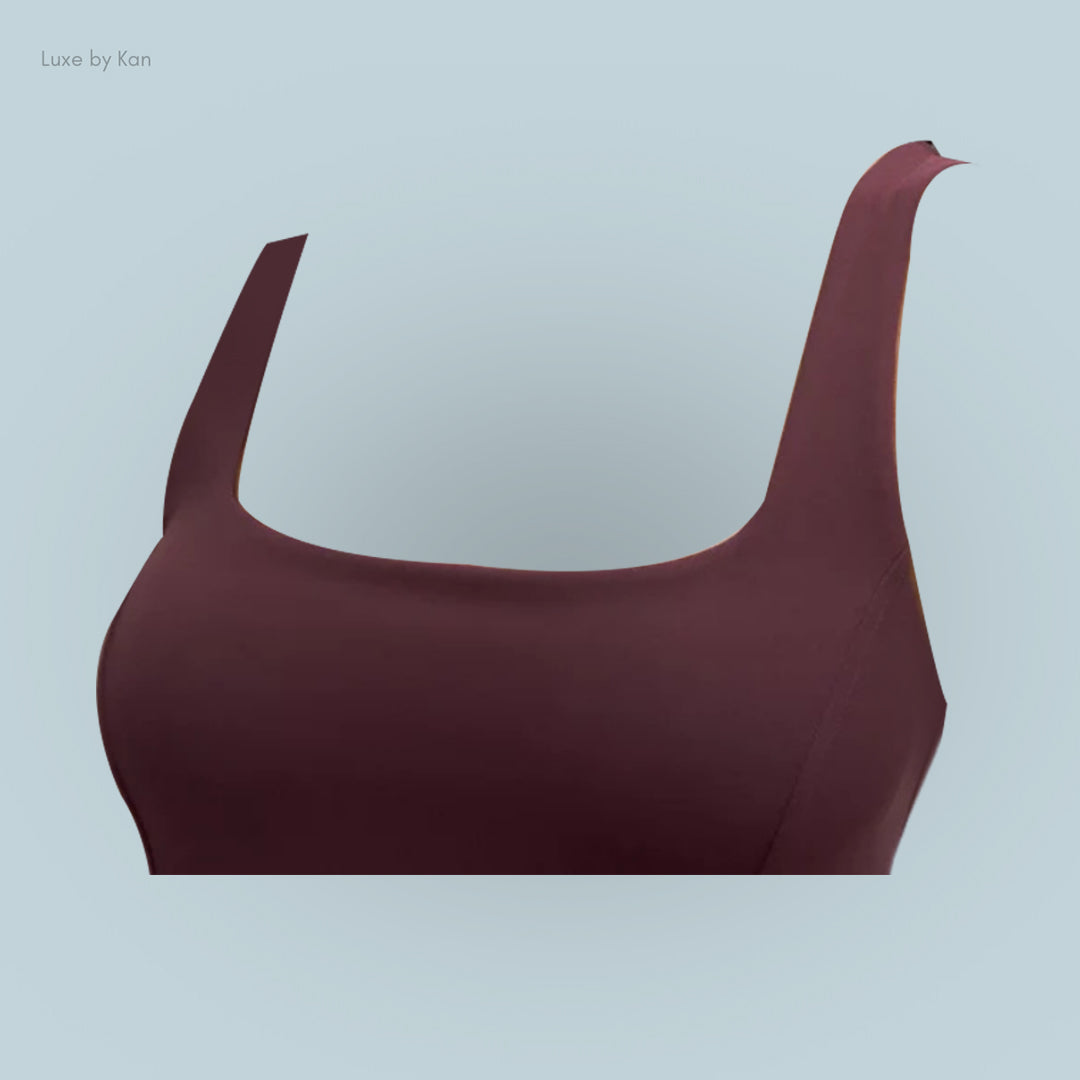 A close-up of a maroon sleeveless top with wide straps, set against a light blue background, featuring a smooth, glossy texture.