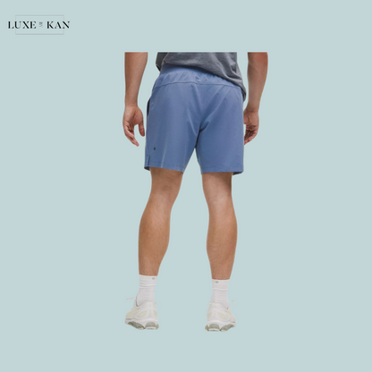 A man wearing a gray t-shirt and blue shorts stands with his back.