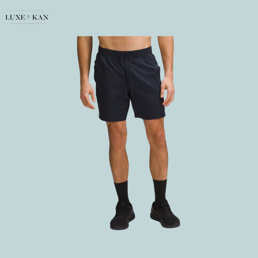 A shirtless man stands wearing black athletic shorts, black socks, and sneakers.