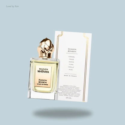 Maison Mataha Évasion Bonbon extrait de parfum in the clear bottle with a gold flower top beside the fragrance notes list card.