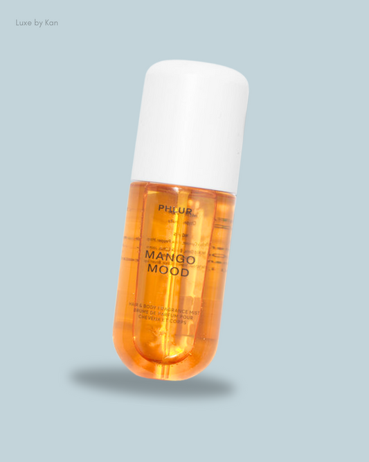 A bottle of "Mango Mood" hair and body mist, featuring an orange liquid and a white cap.