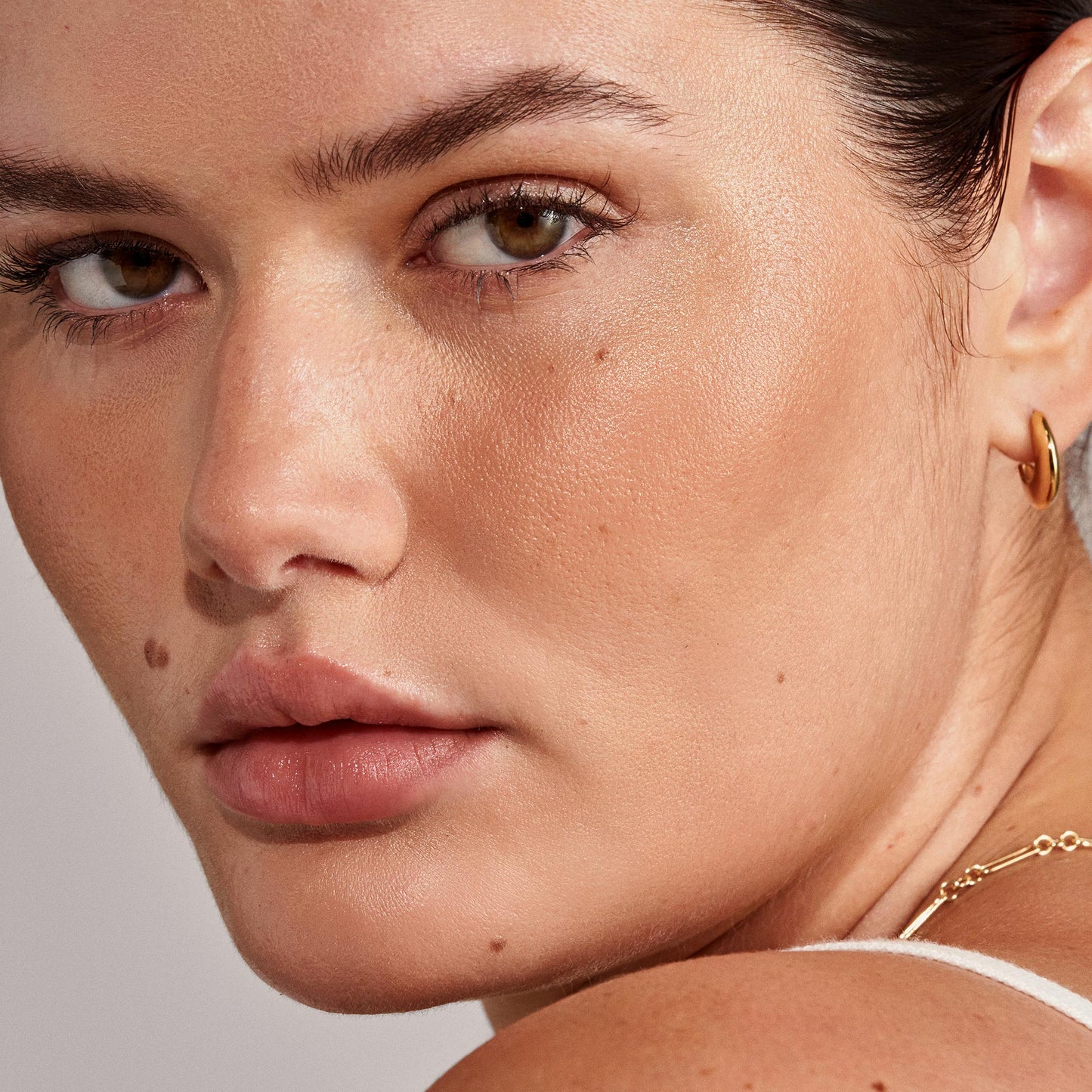 A close-up of a person’s neck and shoulder, showcasing delicate gold jewelry and elegant earrings.