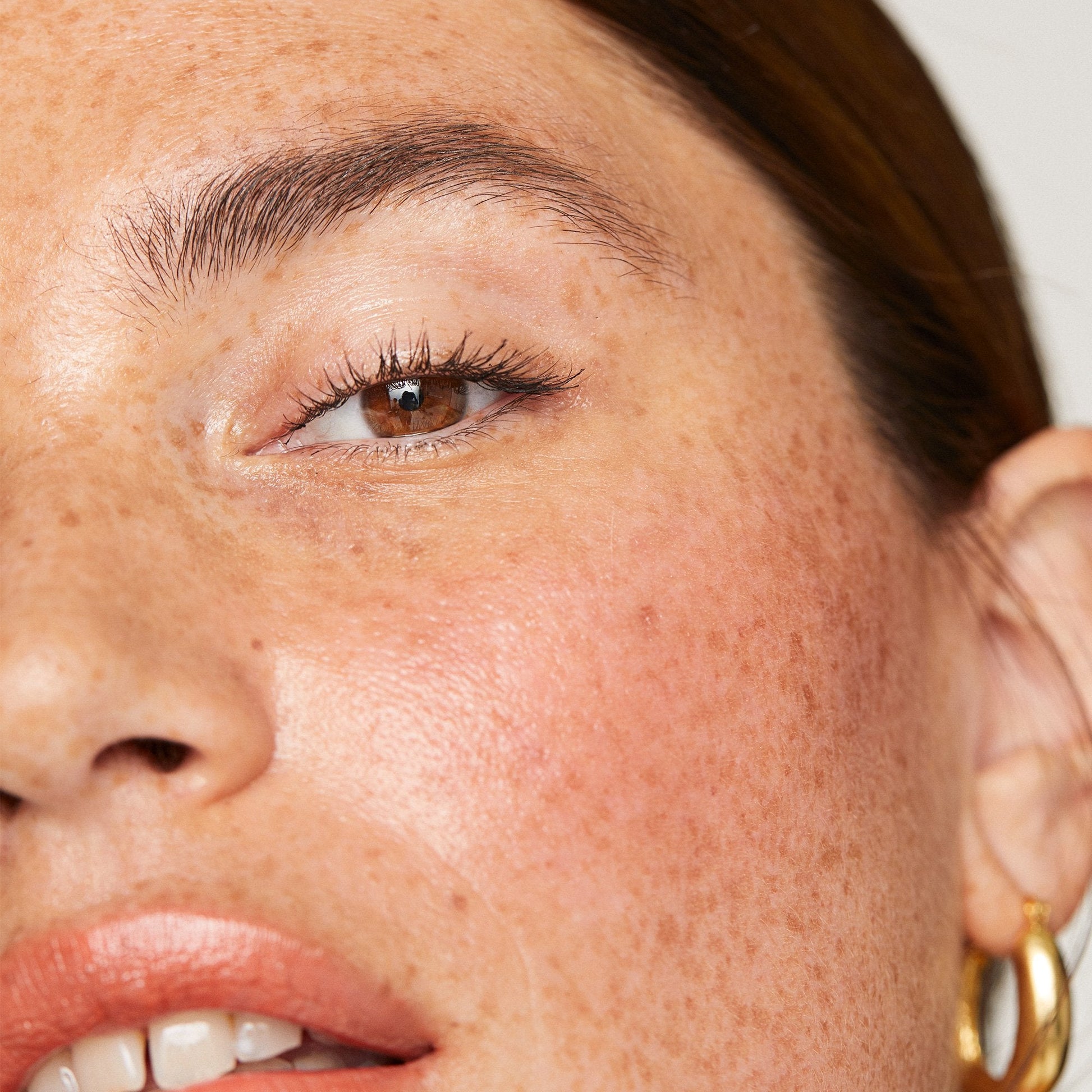 A close-up of a woman's ear adorned with a gold hoop earring, showcasing smooth skin and highlighted hair.