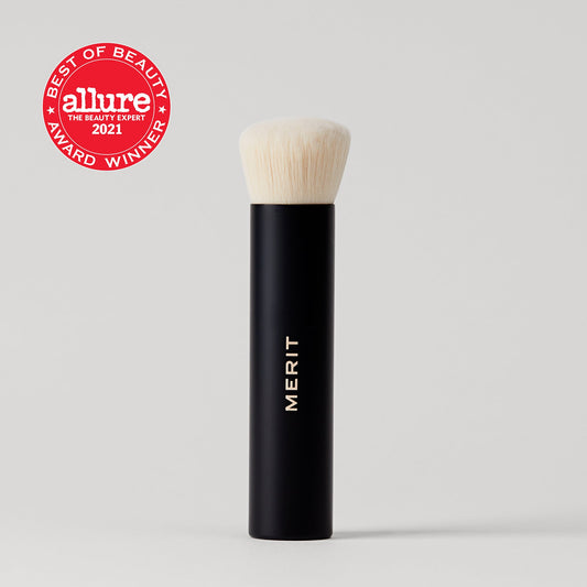 A black makeup brush with a soft white bristle head, labeled "Merit beauty brush no.1 blending brush," next to an award badge for Allure's Best of Beauty 2021.
