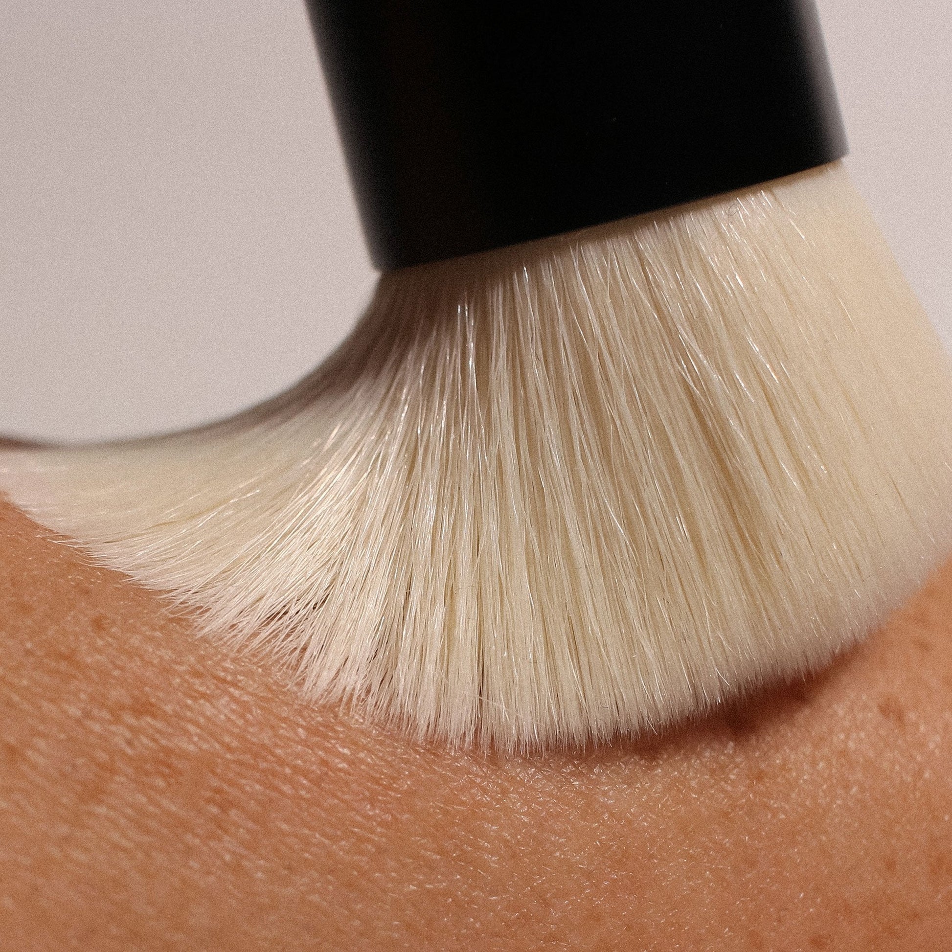 Close-up of a soft makeup brush gliding over a tanned, textured skin surface, showcasing fine bristles in motion.