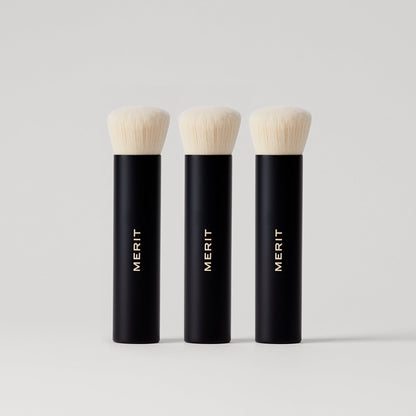 Three black makeup brushes with soft white bristles, labeled "MERIT". 