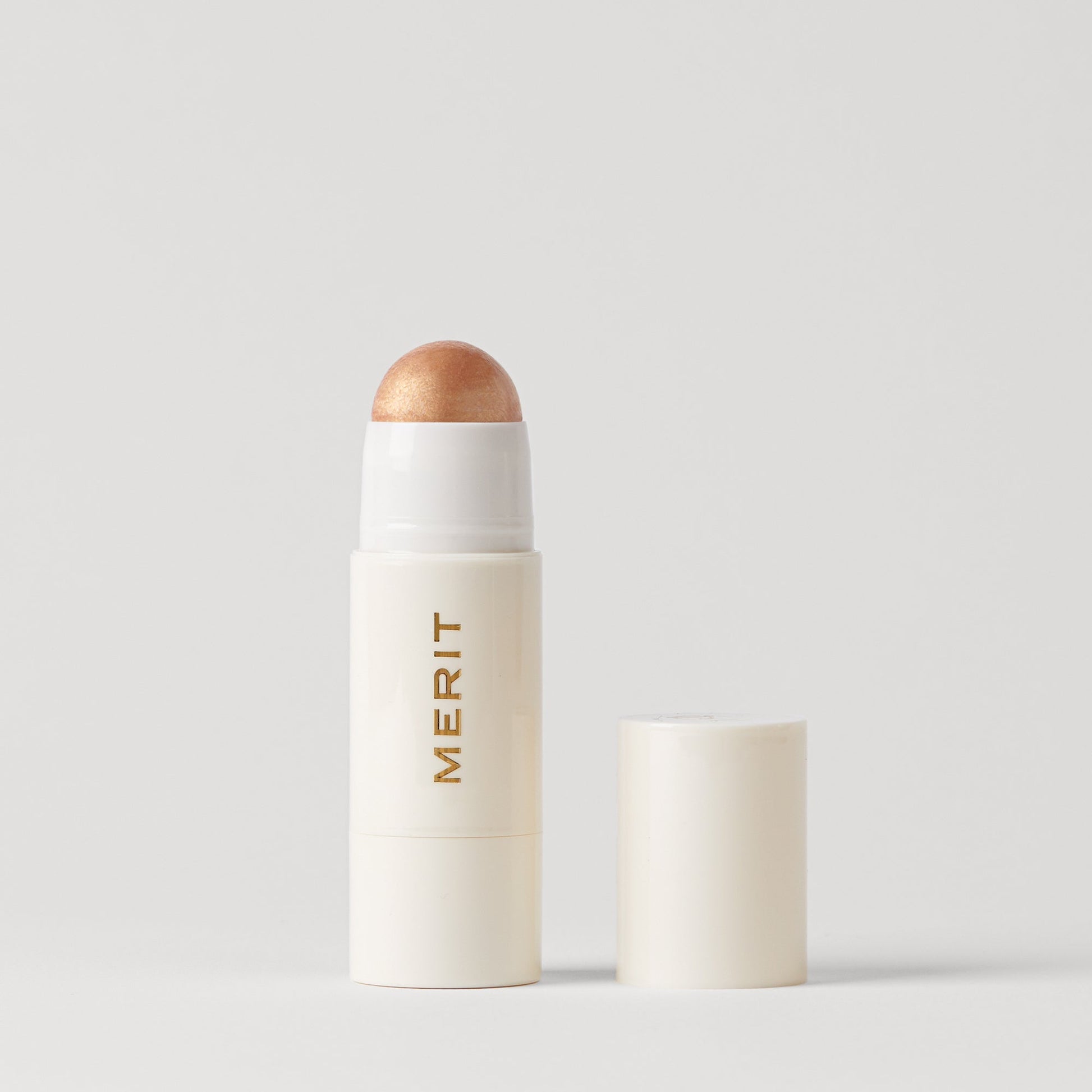 Merit beauty day glow highlighting balm tube with a metallic bronze top, showcasing a minimalist design.