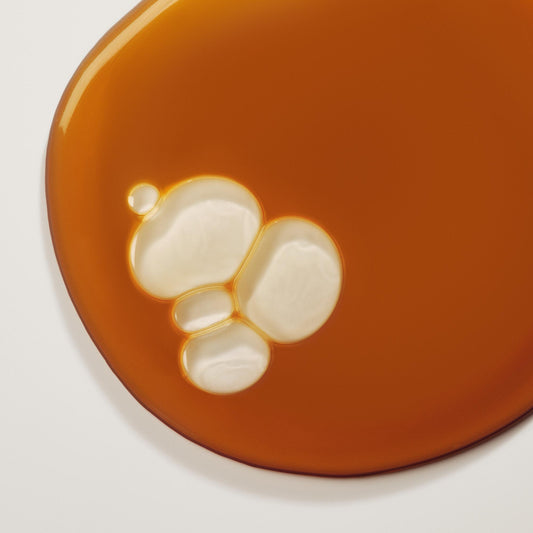 Close-up of a glossy caramel-colored liquid with glossy white bubbles merging into the surface, creating an abstract texture.