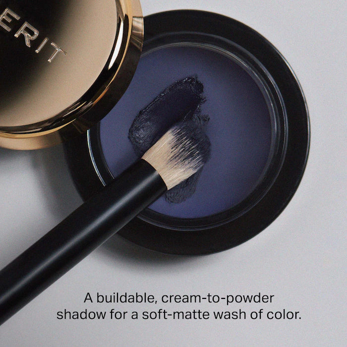 A close-up of a cream-to-powder eyeshadow in a sleek container, with a brush applying a rich, soft-matte purple shade.