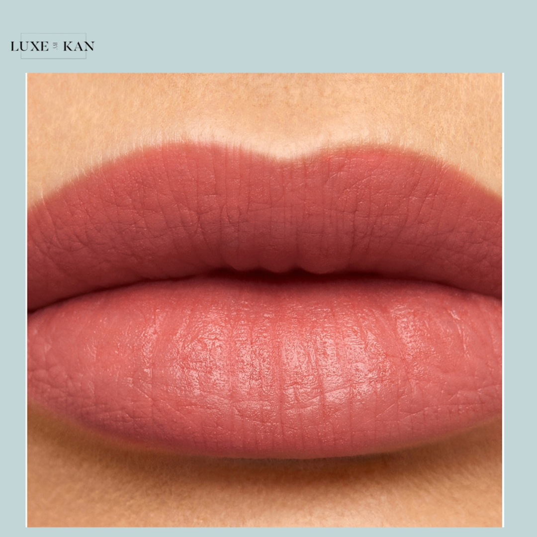 Close-up of full, matte lips in a soft pink shade with a smooth texture, framed by a light blue background, labeled "Luxe x Kan."
