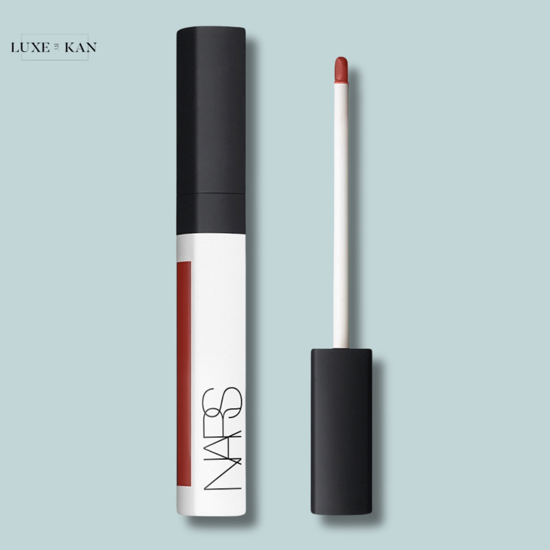 Nars radiant creamy colour corrector tube with a black cap and a white body next to a doe-foot applicator, showcasing a rich red shade.