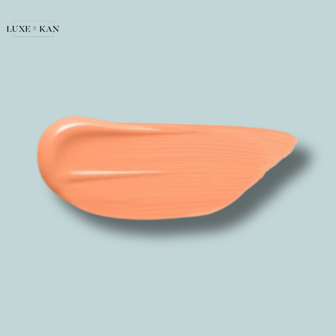 A smooth, peach-colored cream swatch on a soft light blue background, showcasing a glossy finish and even texture.