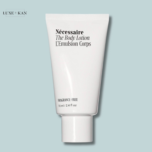 A white tube of Nécessaire The Body Lotion travel size, 70 ml, labeled "fragrance-free," set against a pale blue background.