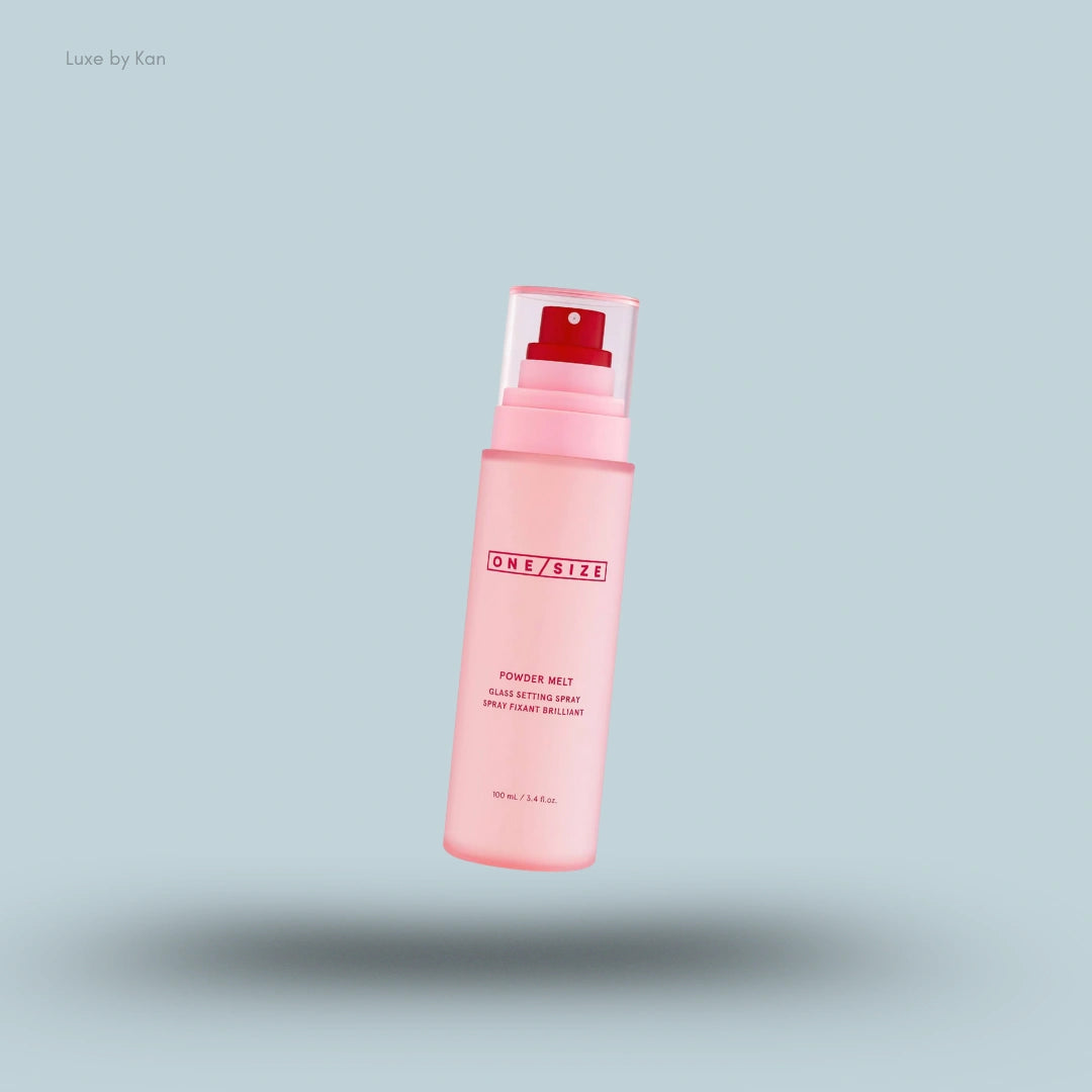 A pink bottle of Onesize Powder Melt Glass Setting Spray with a clear cap and a red sprayer is floating on a light blue background.