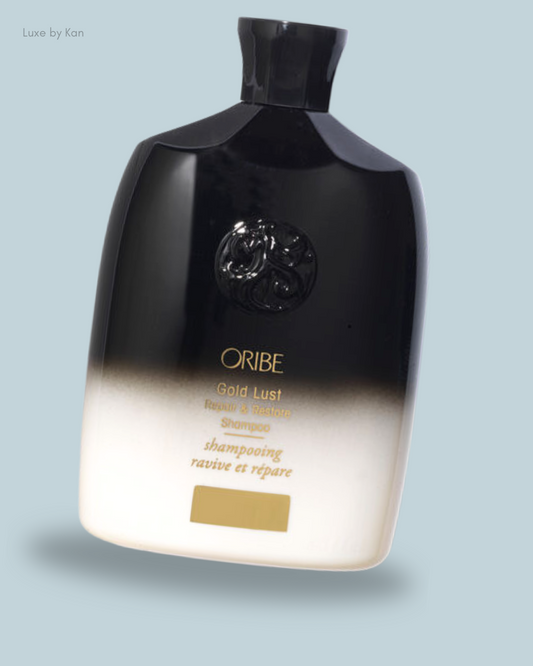 A sleek black and white shampoo bottle labeled "Oribe Gold Lust Repair & Restore Shampoo."