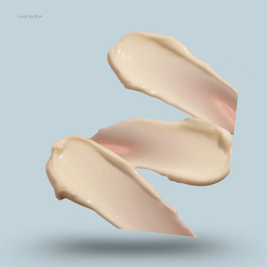 Three glossy streaks of beige moisturiser cream layered in a curved vertical column.