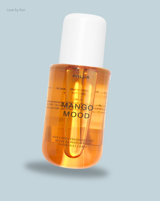 A bottle of PHLUR's Mango Mood hair and body fragrance mist, featuring a vibrant orange liquid and a white cap.