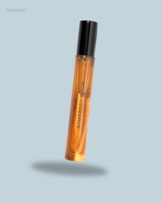 A floating bottle of Luxe by Kan's "Somebody Good" body oil, featuring a sleek black cap and translucent amber liquid.
