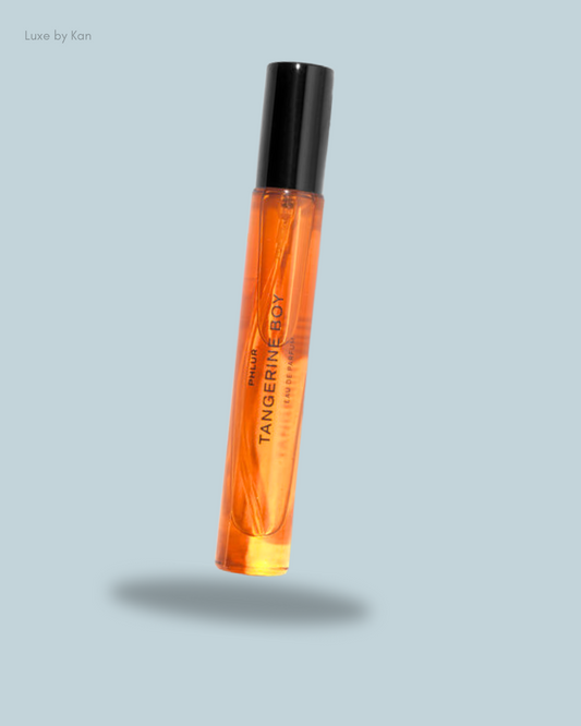 A sleek, orange perfume bottle labeled "Tangerine Boy" with a black cap, floating against a light blue background.