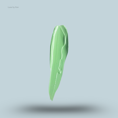 Vertical smear of light green Plouise makeup base against a pale blue background, casting a soft shadow.