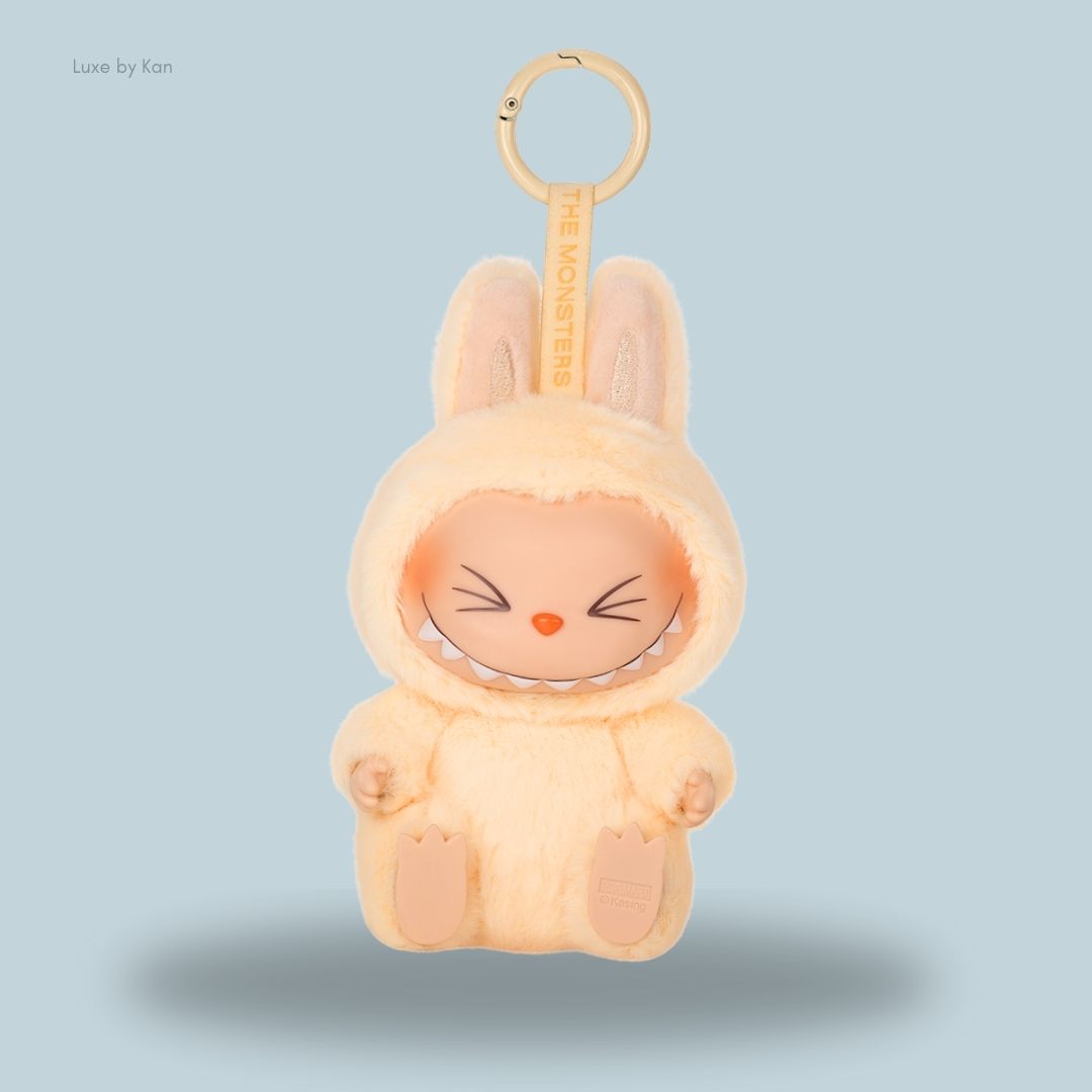 A cute Pop Mart Labubu The Monsters Have a Seat – SISI vinyl plush doll keychain, dressed in a soft yellow bunny suit with a mischievous grin and large ears.