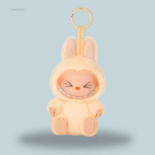 A cute Pop Mart Labubu The Monsters Have a Seat – SISI vinyl plush doll keychain, dressed in a soft yellow bunny suit with a mischievous grin and large ears.
