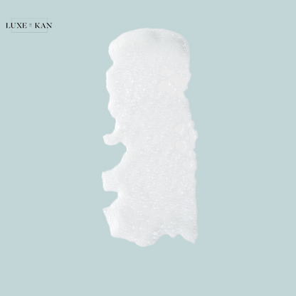 A silky, white cream with a bubbly texture on a soft blue background, branding visible: "LUXE & KAN."