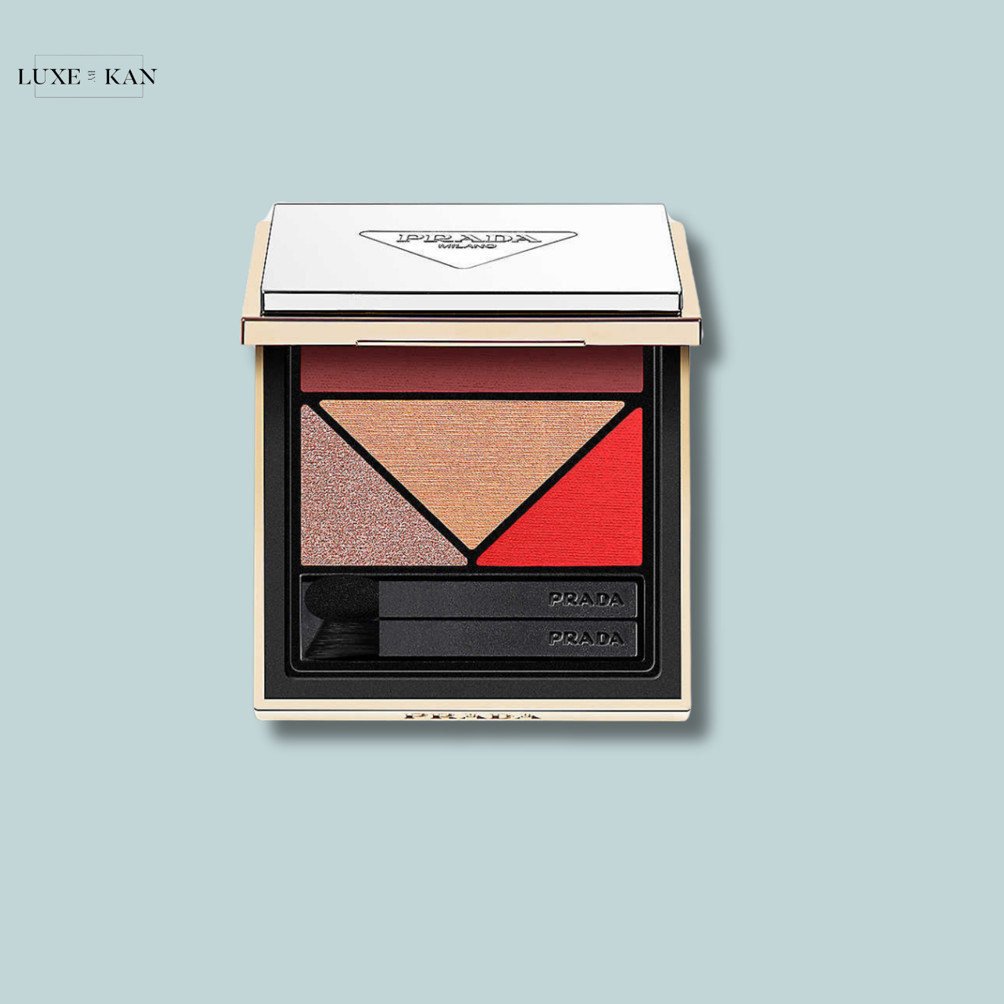 A luxury Prada eyeshadow palette featuring a triangle of shades: warm beige, shimmery copper, and vibrant red, with dual applicators.