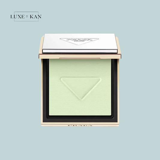 Prada compact powder with a green hue, elegantly displayed against a soft blue background, featuring a reflective silver lid.