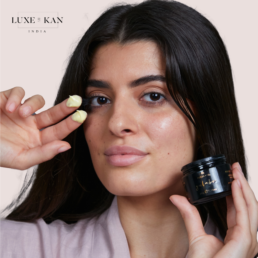 A hand displays two dollops of light yellow cream, while the other hand holds a black jar of gulabo rose & seabuck replenishing face creme.
