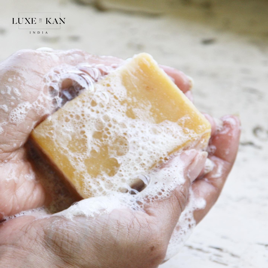 Hands holding a bar of soap, surrounded by bubbles, conveying a sense of cleanliness and indulgence in a natural setting.