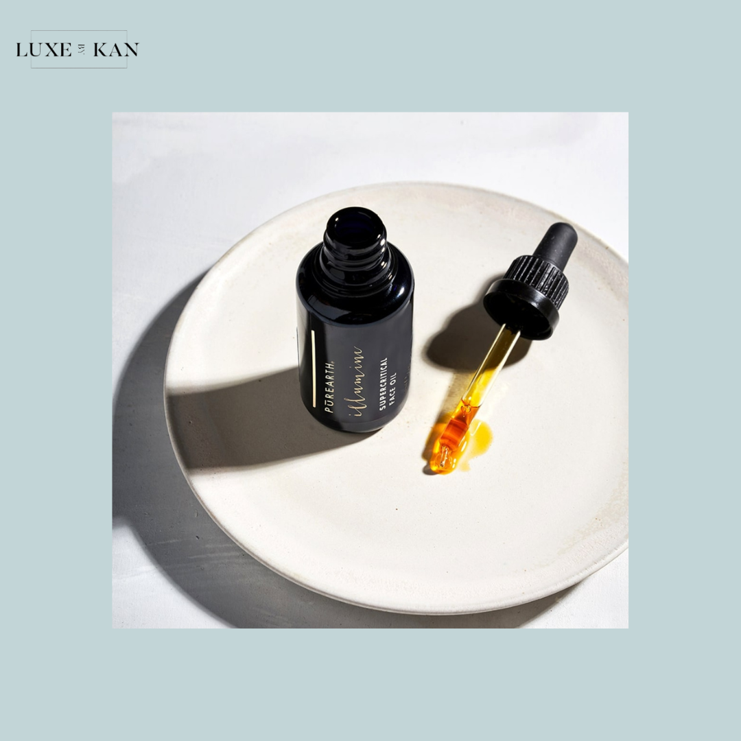 A black dropper bottle labeled "Pure Earth Illumine Supercritical Oil" on a beige plate, with an orange oil droplet beside it.