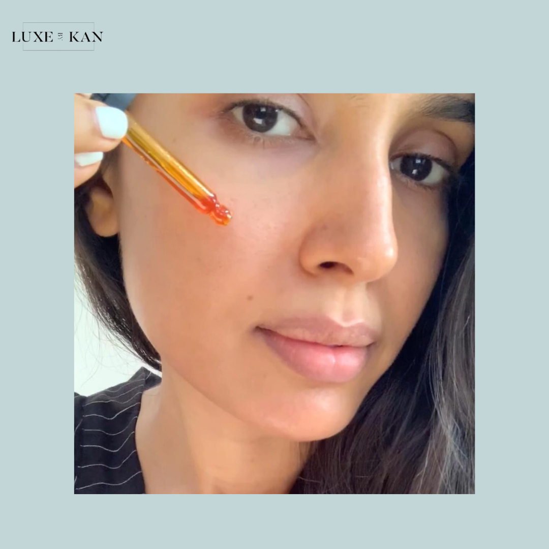 A person applies illumine supercritical face oil while sitting, with long dark hair and wearing a striped shirt.
